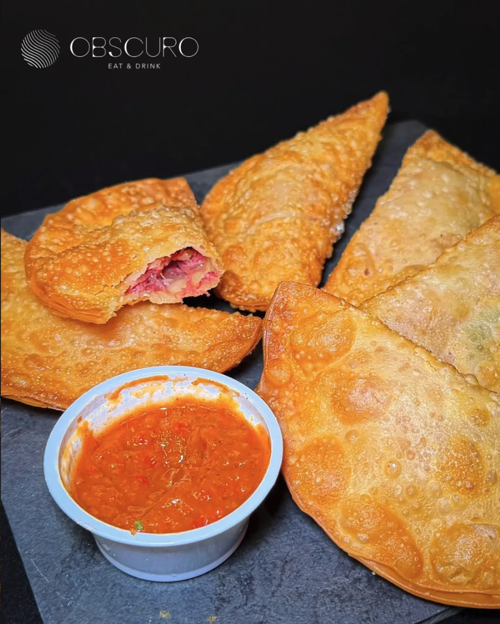 Porção de pastéis de carne seca dourados com molho de pimenta da casa
