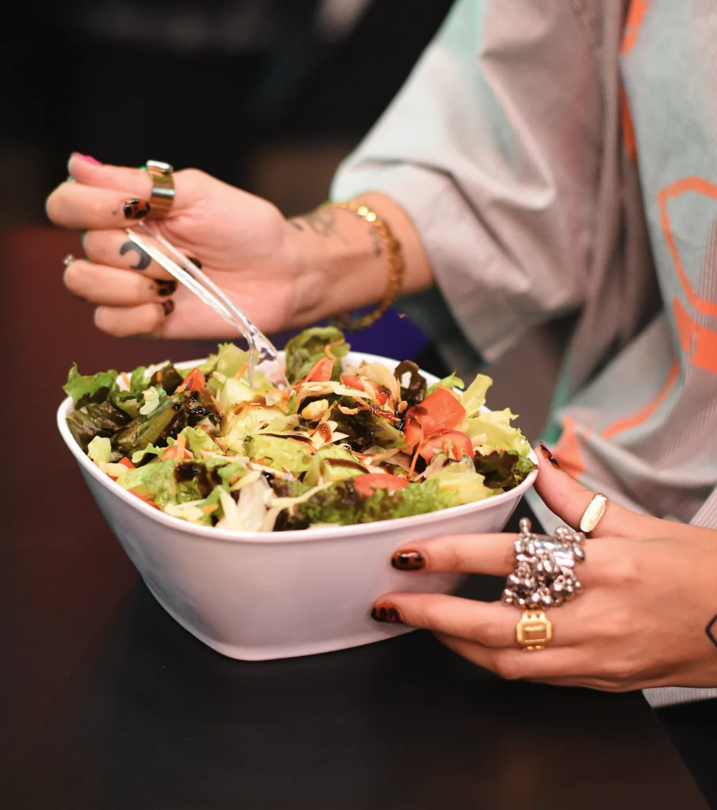 Bowl de salada com tomate e molho balsâmico, mãos com anéis segurando o garfo